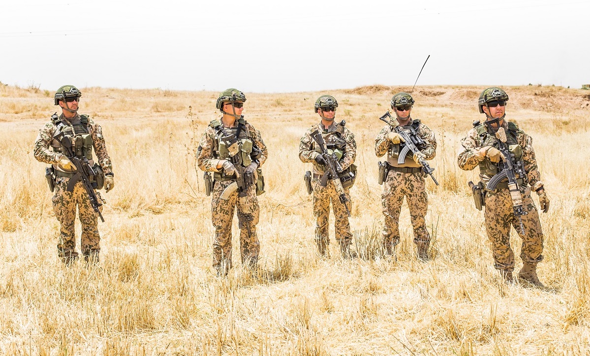Viisi aseistettua maastopukuista sotilasta seisoo ulkona