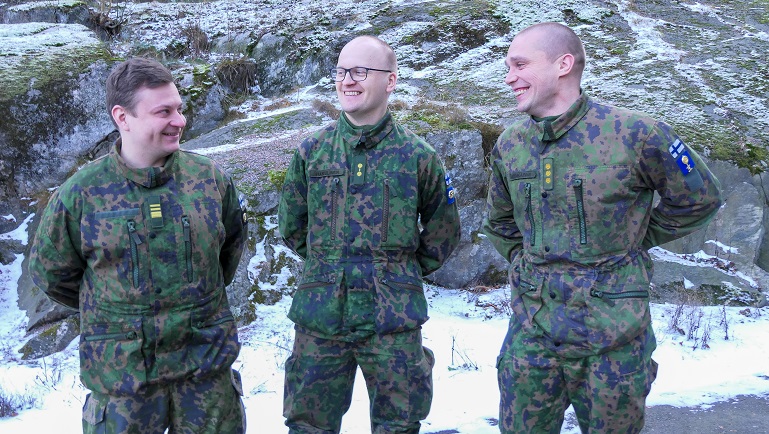 Kolme sotilasta maastopuvuissa seisoo hymyillen ulkona